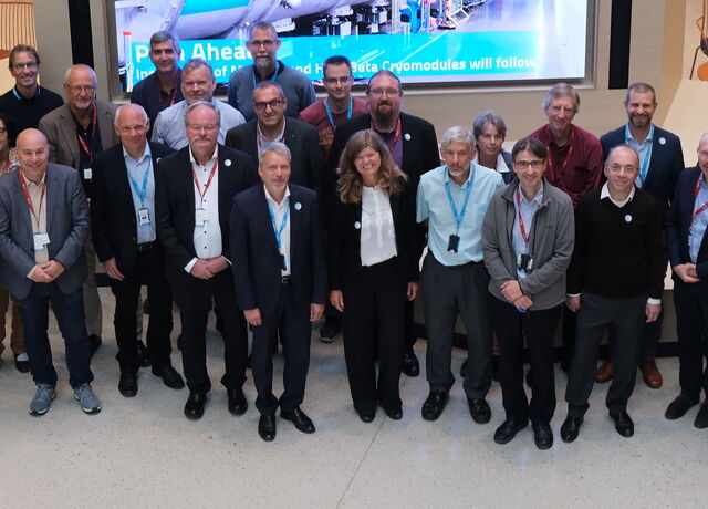 25 members of the LENS meeting stand in front of a screen in the atrium of the ESS offices